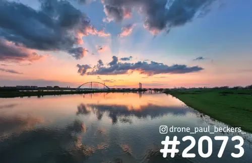 Luchtfoto van de Waal en De Oversteek bij Nijmegen-Lent, met een roze wolkenlucht die weerspiegelt in het water