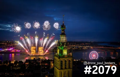 Luchtfoto van vuurwerk boven de Waal in Nijmegen, met de verlichte Stevenskerk en een reuzenrad bij avond