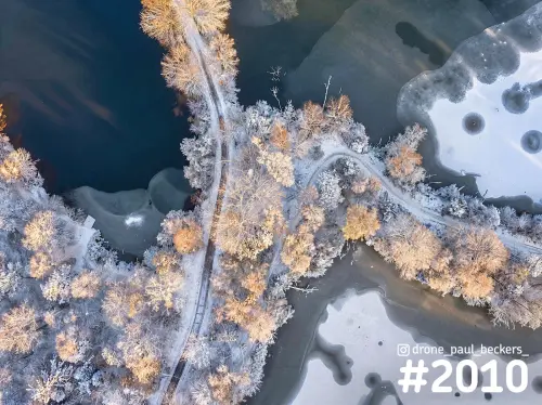 Luchtfoto van boven op berijpte bomen en een pad tussen deels bevroren water bij Beek-Ubbergen, in warm winterlicht