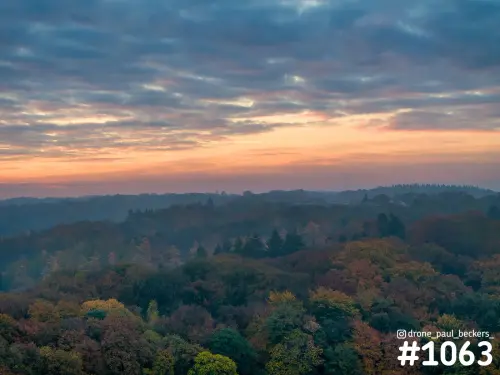Luchtfoto van herfstbos bij Beek-Ubbergen met gele en rode bladeren onder een oranje avondrood en gelaagde wolken
