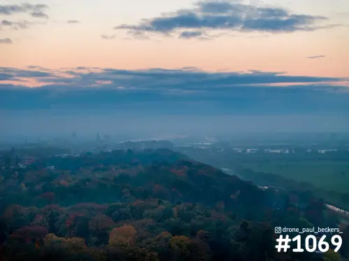 Luchtfoto van herfstbomen bij Beek-Ubbergen met nevel over de vallei en een roze avondgloed boven Nijmegen in de verte