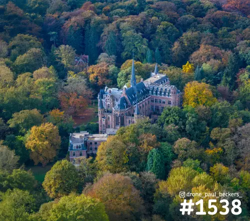 Luchtfoto van een kasteel met spitse toren tussen herfstbomen in Beek-Ubbergen, met geel en rood bladerdak eromheen