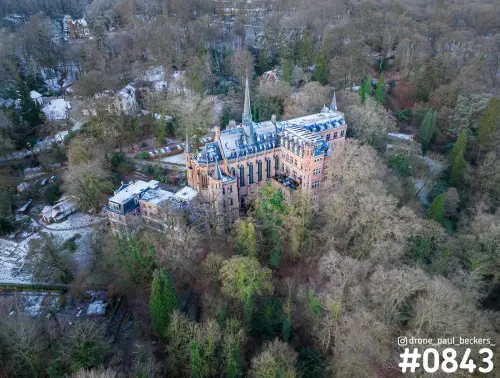Luchtfoto van een kasteel met torenspitsen tussen kale bomen in Beek-Ubbergen, met een laagje sneeuw op daken en grond