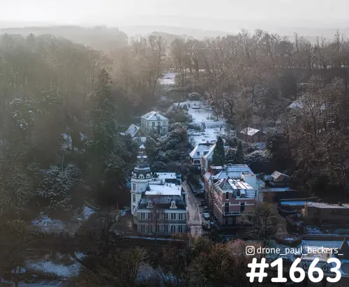 Luchtfoto van Beek-Ubbergen met een besneeuwd dorpje tussen bomen, een villa met torentje en mist in het zachte licht