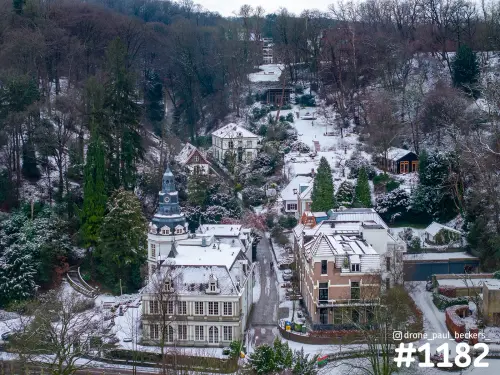 Luchtfoto van villa's met besneeuwde daken in Beek-Ubbergen, aan een smalle weg langs de beboste heuvel