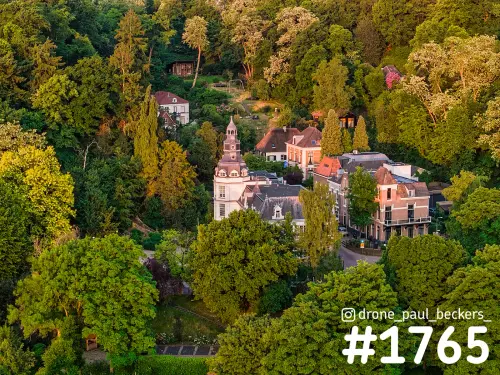 Luchtfoto van villa's en een wit torentje tussen groene bomen in Beek-Ubbergen, in warm avondlicht in het voorjaar