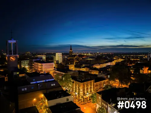 Luchtfoto van het centrum van Nijmegen in het blauwe uur, met verlichte terrassen en een klokkentoren links