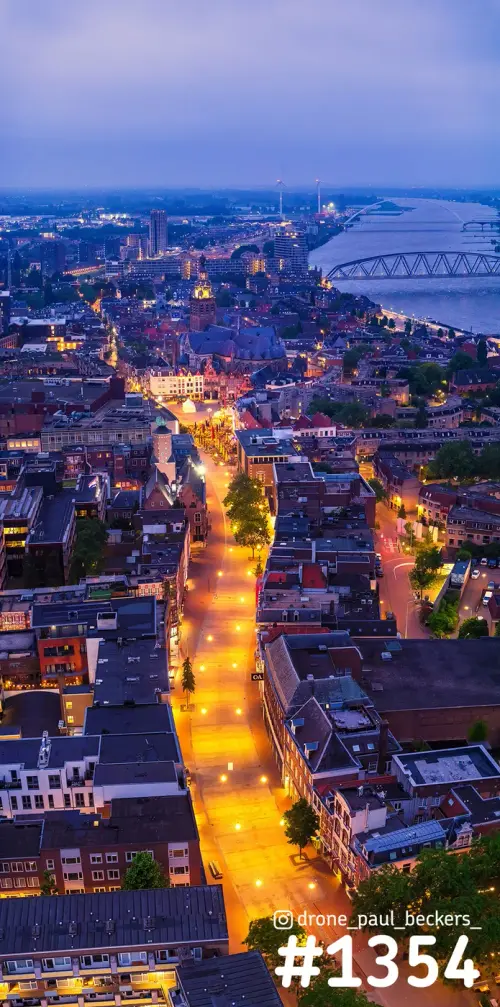Luchtfoto van het centrum van Nijmegen in het blauwe uur, met verlichte straat, Stevenskerk en de Waal met brug