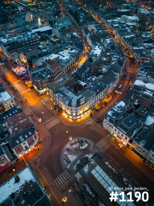 Luchtfoto van een kruispunt in het centrum van Nijmegen in de avond, met sneeuw op de daken en oranje straatverlichting