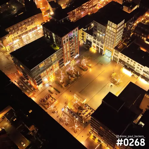 Luchtfoto van een verlicht plein in het centrum van Nijmegen 's avonds, met verlichte bomen en terrassen tussen woonblokken