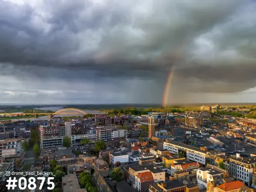 Luchtfoto van het centrum van Nijmegen met regenboog onder een donkere regenwolk en de Waalbrug links aan de rivier