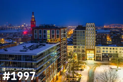 Luchtfoto van het centrum van Nijmegen in de sneeuw bij avondlicht, met de Stevenskerk en de Waalbrug in de verte