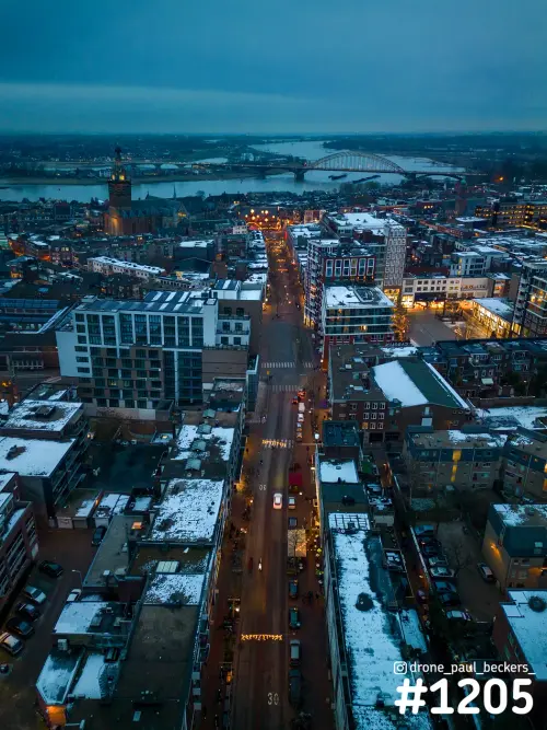 Luchtfoto van het centrum van Nijmegen in de schemering, sneeuw op daken en een straat richting de Waalbrug