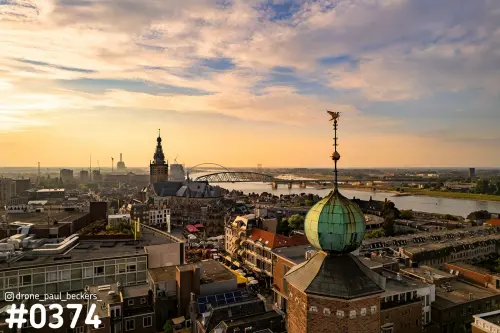 Luchtfoto van het centrum van Nijmegen in avondlicht, met Stevenskerk, de Waal en een groene koepel met windvaan