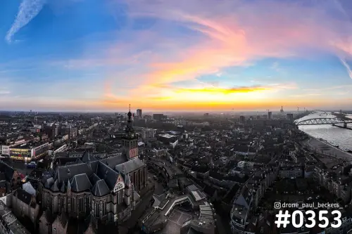 Luchtfoto van het centrum van Nijmegen met de Stevenskerk op de voorgrond en de Waal rechts, onder een roze en oranje lucht