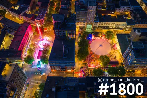 Luchtfoto van het centrum van Nijmegen bij avond tijdens de Vierdaagse, met een verlichte attractie en ronde witte tent