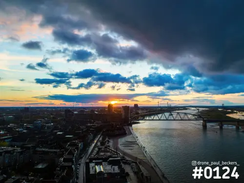 Luchtfoto van het centrum van Nijmegen en de Waal bij zonsondergang, met donkere wolken en De Oversteek in de verte