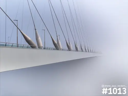 Luchtfoto van De Oversteek in Nijmegen in dichte mist, met witte brugdek en tuikabels die in het grijs verdwijnen