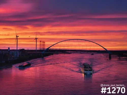Luchtfoto van De Oversteek over de Waal in Nijmegen na zonsondergang, met een rivierboot en vrachtschip op het roze water