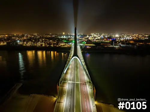 Luchtfoto van De Oversteek over de Waal in Nijmegen bij nacht, met verlichte pyloon en stadslichten op de oever