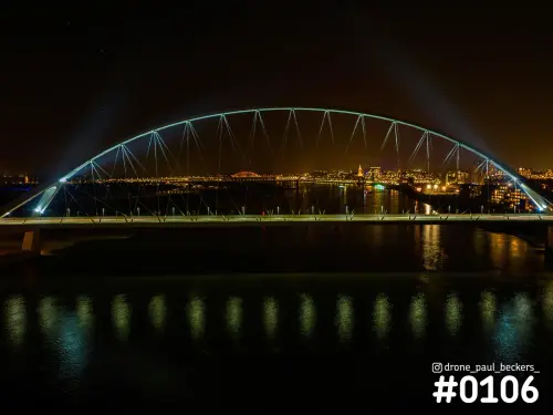 Luchtfoto van De Oversteek in Nijmegen 's nachts, met de verlichte boog boven de Waal en de stad met Stevenskerk op de achtergrond