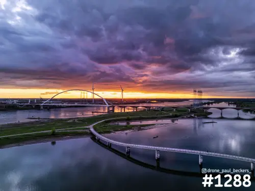 Luchtfoto van De Oversteek en de Waal bij Nijmegen met zonsondergang, paarse wolken en een fiets- en wandelbrug over de nevengeul