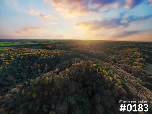 Luchtfoto van de Duivelsberg bij Nijmegen met herfstkleuren in het bos en een laagstaande zon achter gekleurde wolken