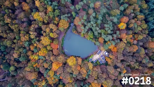Luchtfoto van de Duivelsberg bij Nijmegen in de herfst: vijver met kleine gebouwtjes in een bos vol oranje en groene bomen