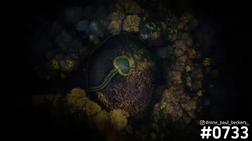 Luchtfoto recht van boven van de Duivelsberg in avondlicht, met een kleine vijver in een donkere open plek in herfstbos