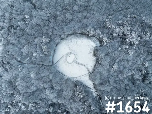Luchtfoto van besneeuwd bos op de Duivelsberg bij Nijmegen, met een witte open plek en kronkelende paadjes erdoorheen