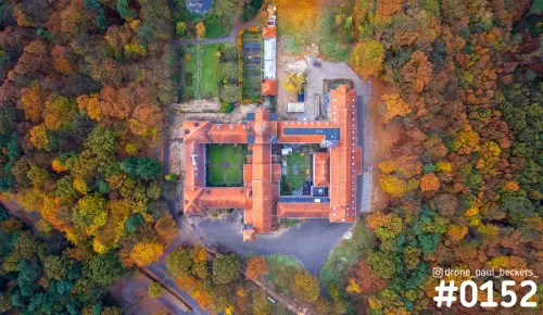 Luchtfoto van boven op een gebouwencomplex met oranje daken en binnentuinen, omringd door herfstbos in geel en oranje