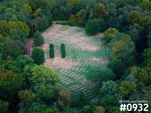 Luchtfoto van een begraafplaats bij de Goffert in Nijmegen met rijen witte grafstenen en twee cipressen tussen het bos