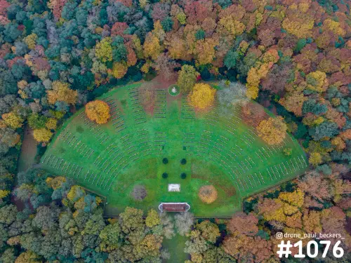 Luchtfoto van een halfronde grasvlakte met rijen witte stenen, omringd door herfstbos bij de Goffert in Nijmegen