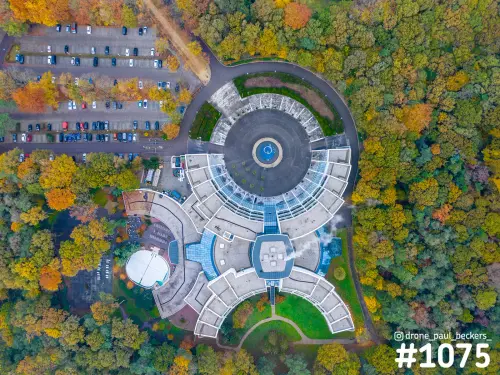 Luchtfoto van boven van een rond gebouw bij de Goffert in Nijmegen, omringd door herfstbos en met parkeerplaats