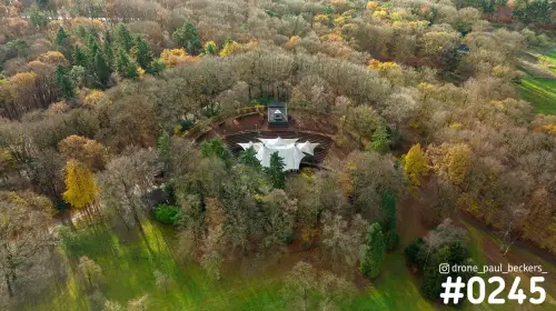 Luchtfoto van een openluchttheater met wit zeildak tussen herfstbomen bij de Goffert in Nijmegen, met gele bladeren