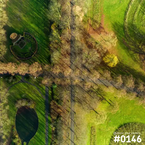 Luchtfoto recht van boven op een park bij de Goffert in Nijmegen, met lange schaduwen van kale bomen op gras en paden