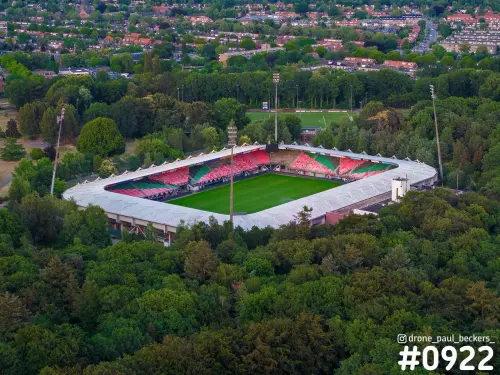 Luchtfoto van het stadion op de Goffert in Nijmegen, omringd door bomen, met rood-groene tribunes en een groen veld