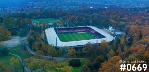 Luchtfoto van stadion De Goffert in Nijmegen in de herfst, met rode tribunestoelen en kleurende bomen rondom het veld