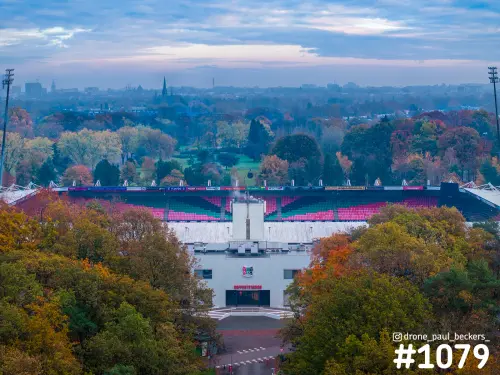 Luchtfoto van het stadion bij de Goffert in Nijmegen in de herfst, met kleurrijke bomen en roze en groene tribunes