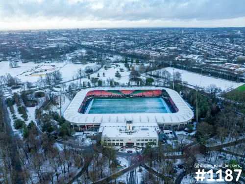 Luchtfoto van het stadion bij de Goffert in Nijmegen onder sneeuw, met wit dak rond het groene veld en kale bomen