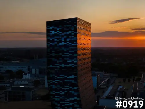 Luchtfoto van een hoogbouwtoren bij de Goffert in Nijmegen tijdens zonsondergang, met oranje weerkaatsing op de gevel