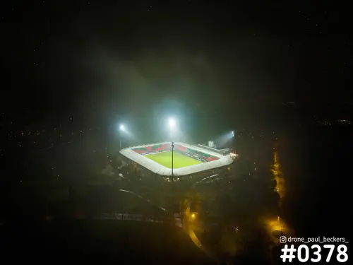 Luchtfoto van het Goffertstadion in Nijmegen 's avonds, met felle lichtmasten en mist rond het verlichte groene veld