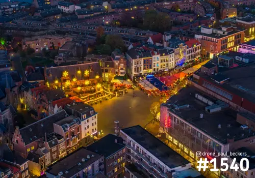 Luchtfoto van de Grote Markt in Nijmegen in de schemering, met kerstverlichting op de gevel en gekleurde marktkraampjes