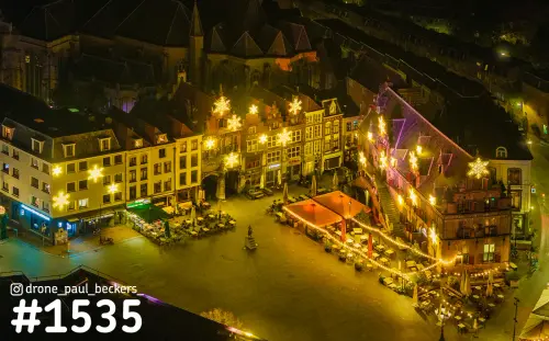 Luchtfoto van de Grote Markt in Nijmegen 's avonds, met verlichte sterren op de gevels en terrassen met oranje tenten