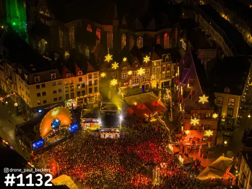 Luchtfoto van de Grote Markt in Nijmegen 's avonds, vol publiek voor een podium en lichtsterren tussen de gevels, Stevenskerk erachter