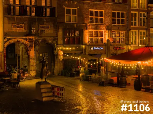 Grote Markt in Nijmegen 's avonds met glanzende keien, lichtslingers boven terrassen en een beeld op een sokkel