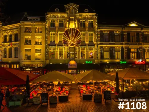 Grote Markt in Nijmegen bij avond met verlichte gevels, een grote ronde lichtdecoratie en terrassen met parasols