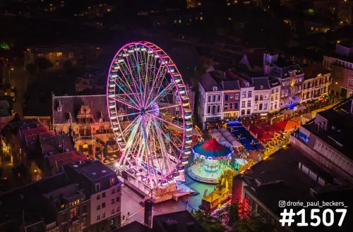 Luchtfoto van het reuzenrad en de draaimolen op de Grote Markt in Nijmegen tijdens de kermis, verlicht in de avond