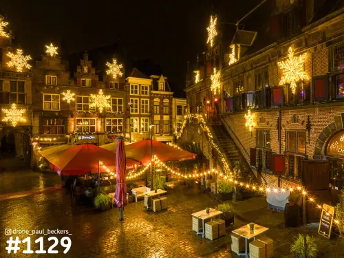 Luchtfoto van de Grote Markt in Nijmegen 's avonds met lichtgevende sneeuwvlokken en rode parasols op het terras