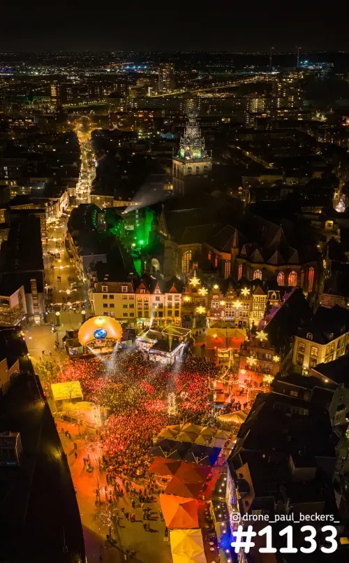 Luchtfoto van de Grote Markt in Nijmegen bij nacht, met een rood verlichte menigte en de groen aangelichte Stevenskerk
